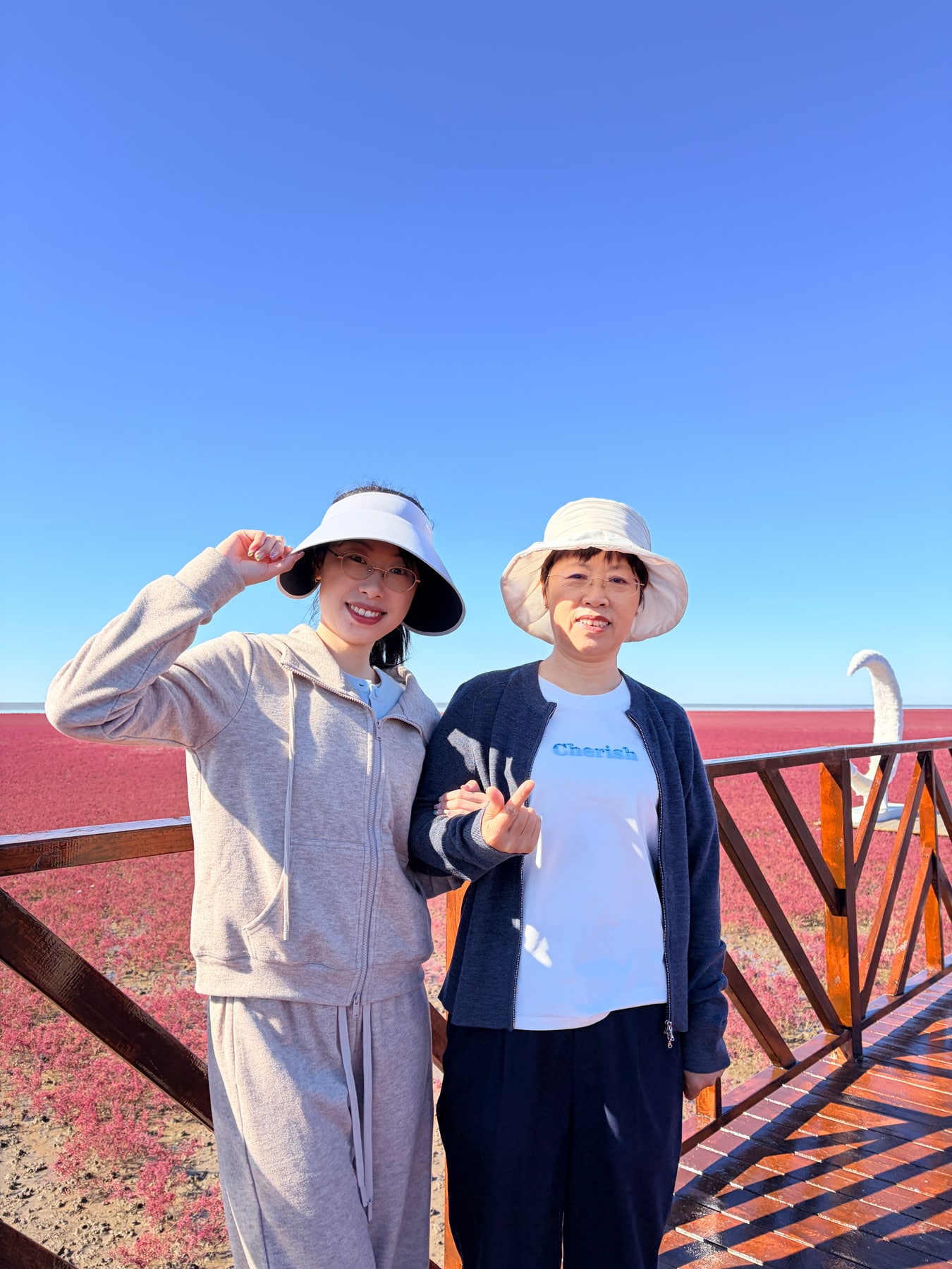妈妈和女儿挽着手臂在红海滩前合影